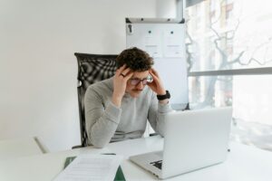 Young man concentrating on work at a desk with laptop in modern office setting.